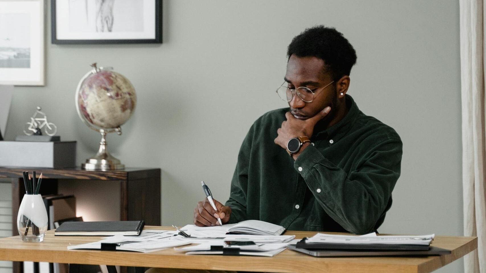 A Man in Black Long Sleeves Sitting while Writing on Table
